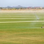 Multiple sprinklers watering a large grassy field