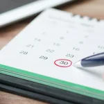 Hand circling a date on a desk calendar